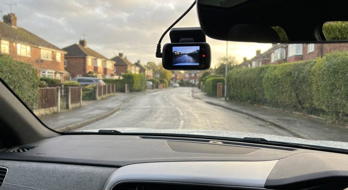 A dash cam mounted on a car windscreen overlooking a quiet British road in soft morning light, viewed from inside the vehicle.